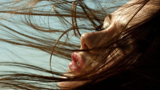 Close-up of a woman's face with flowing hair in natural light against a clear sky background