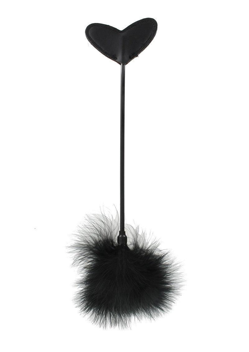 Black heart-shaped leather paddle with a long handle and a fluffy feather end on white background